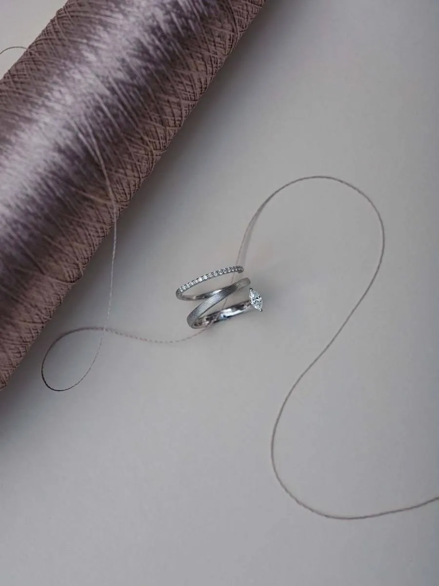 A silver ring beside a silk bobbin and curving threads